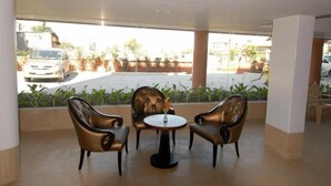 Un área de descanso con dos sillones de cuero y una mesita, una ventana con vistas a coches aparcados y vegetación.