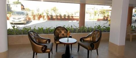 A seating area with two leather chairs and a small table, a window with a view of parked cars and greenery outside.