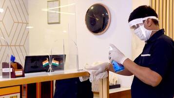A person in a uniform cleaning a counter with a spray bottle, a framed certificate, and a clock on the wall.