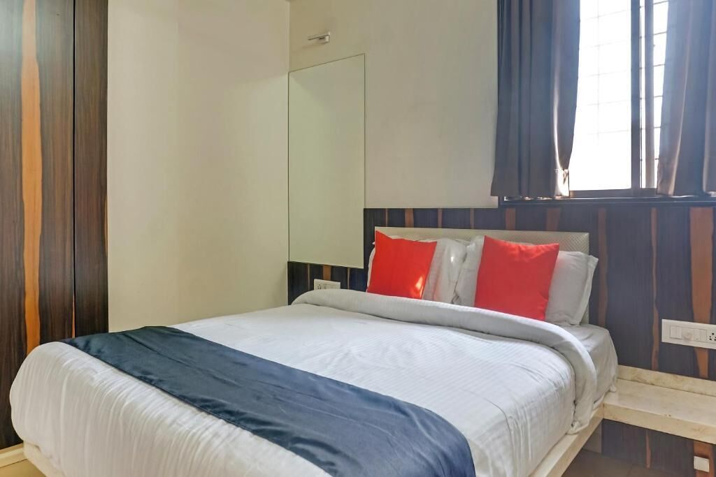A neatly made bed with a white and blue bedspread, a wooden headboard, and red pillows.