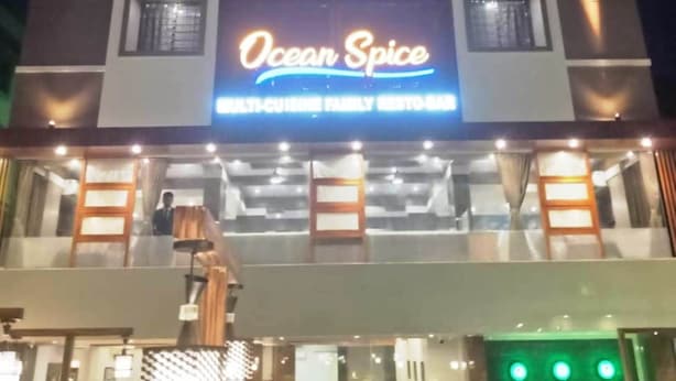 Un restaurante familiar de cocina variada llamado "Ocean Spice", con un diseño arquitectónico moderno, destacando un letrero iluminado y amplias ventanas.
