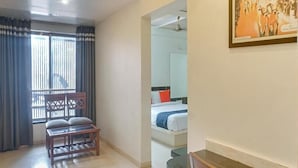 Una habitación de hotel con cama, una silla, ventana con cortinas y un cuadro en la pared.