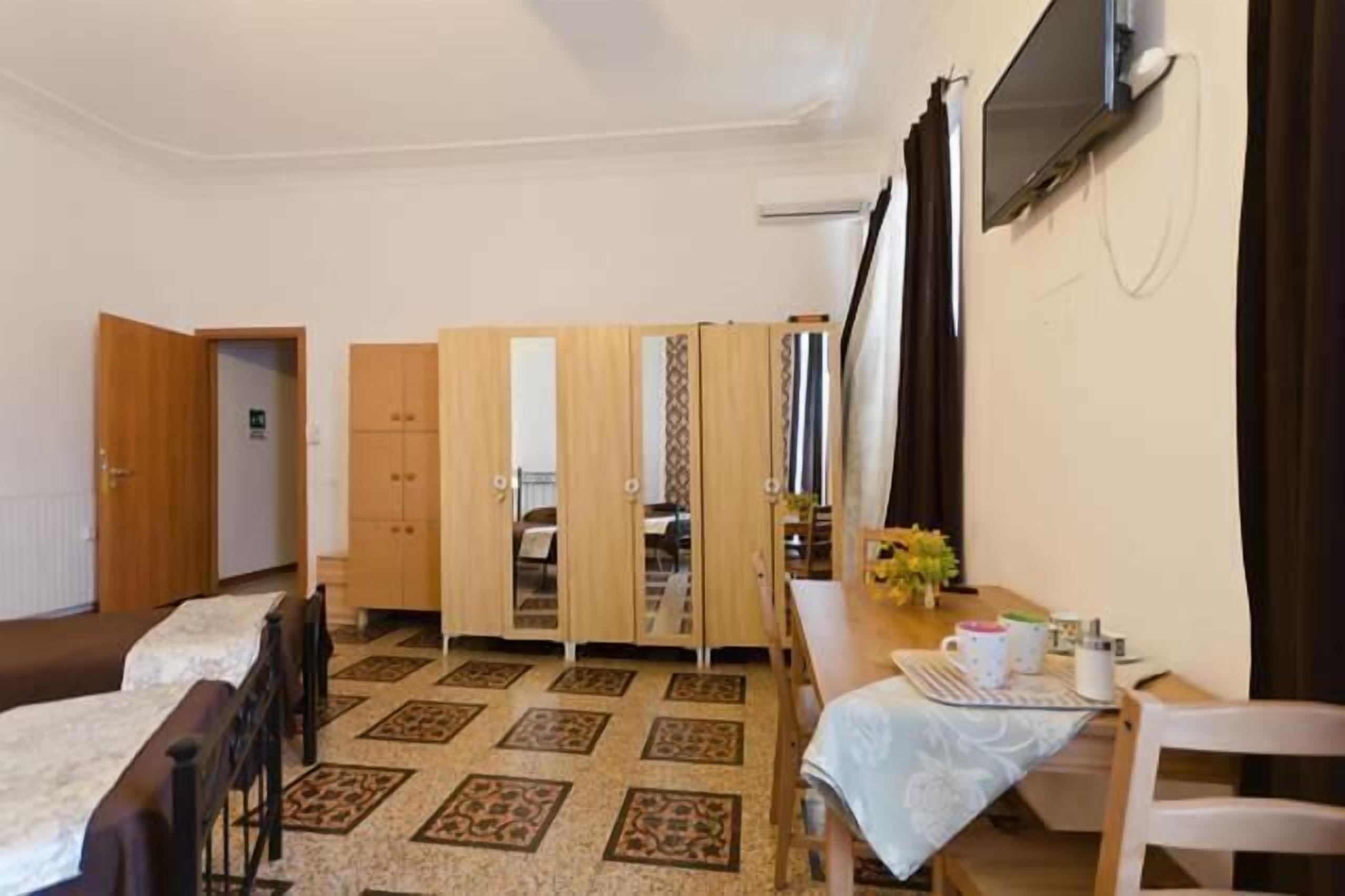 A bedroom with a bed, a wardrobe, a desk with a chair, and a TV mounted on the wall.