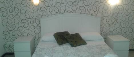 A hotel room with a floral-patterned bedspread, two pillows, two bedside tables, and two wall-mounted lights.
