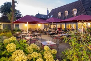 An outdoor dining area with tables and chairs, surrounded by plants and umbrellas.