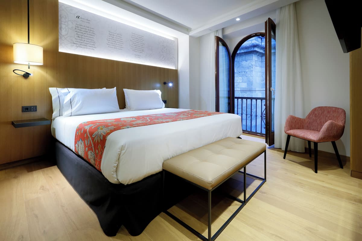 Ein modernes Hotelzimmer mit einem großen Bett, einer Bank, einem roten Sessel und einem Balkon mit Blick.
