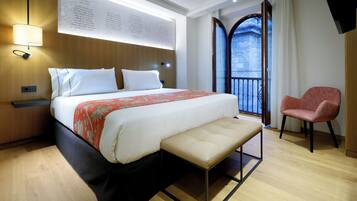 Habitación de hotel moderna con una cama grande, un banco, una silla roja y un balcón con vistas.