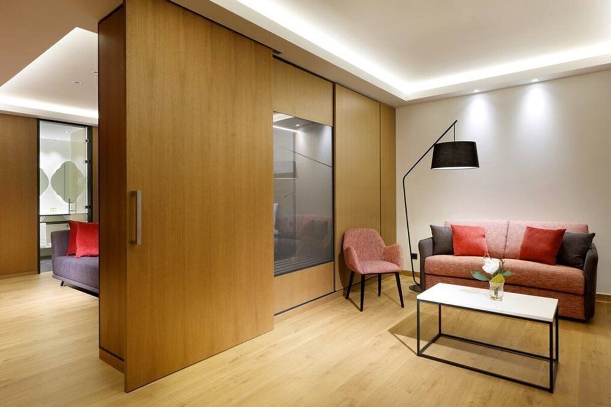 Ein modernes Wohnzimmer mit einer Holztür, die sich verschiebt, einem Sofa mit roten Kissen, einem rosafarbenen Sessel, einem weißen Couchtisch und einer Stehlampe.