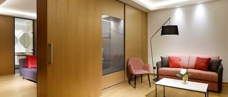 Una sala de estar moderna con una puerta corredera de madera, un sofá con cojines rojos, una silla rosa, una mesa de centro blanca y una lámpara de pie.