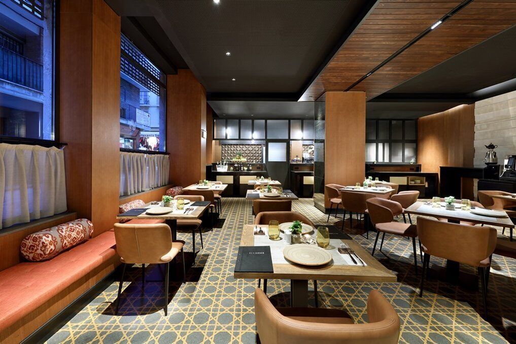 A restaurant with multiple tables and chairs, a patterned floor, and large windows with curtains.