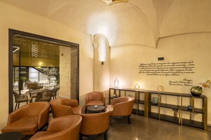Un vestíbulo con sillones de cuero, una pequeña mesa redonda, una consola con objetos decorativos y una pared con una cita.