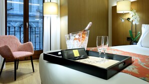 A hotel room with a bed, a chair, a tray with a bottle of champagne, two glasses, and a small card. - Áurea Catedral by Eurostars Hotel Company (Granada)