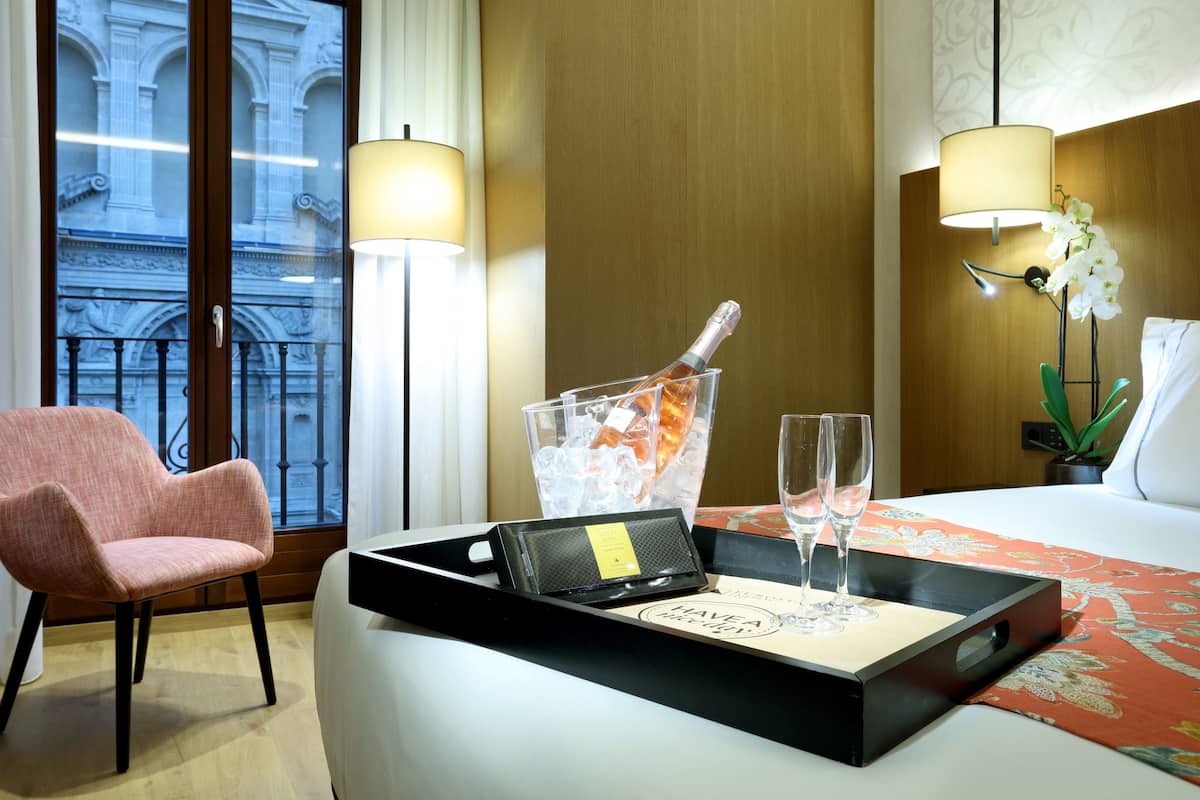 Ein Hotelzimmer mit einem Bett, einem Sessel, einem Tablett mit einer Champagnerflasche, zwei Gläsern und einer kleinen Karte.