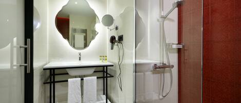Un baño moderno con ducha envuelta en vidrio, un lavabo blanco con espejo y una estantería metálica negra con toallas.