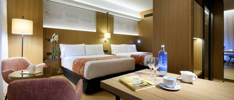 Une chambre d’hôtel comprenant un lit, deux tables de chevet, un bureau avec une chaise, une petite table avec une chaise et une plante en pot.