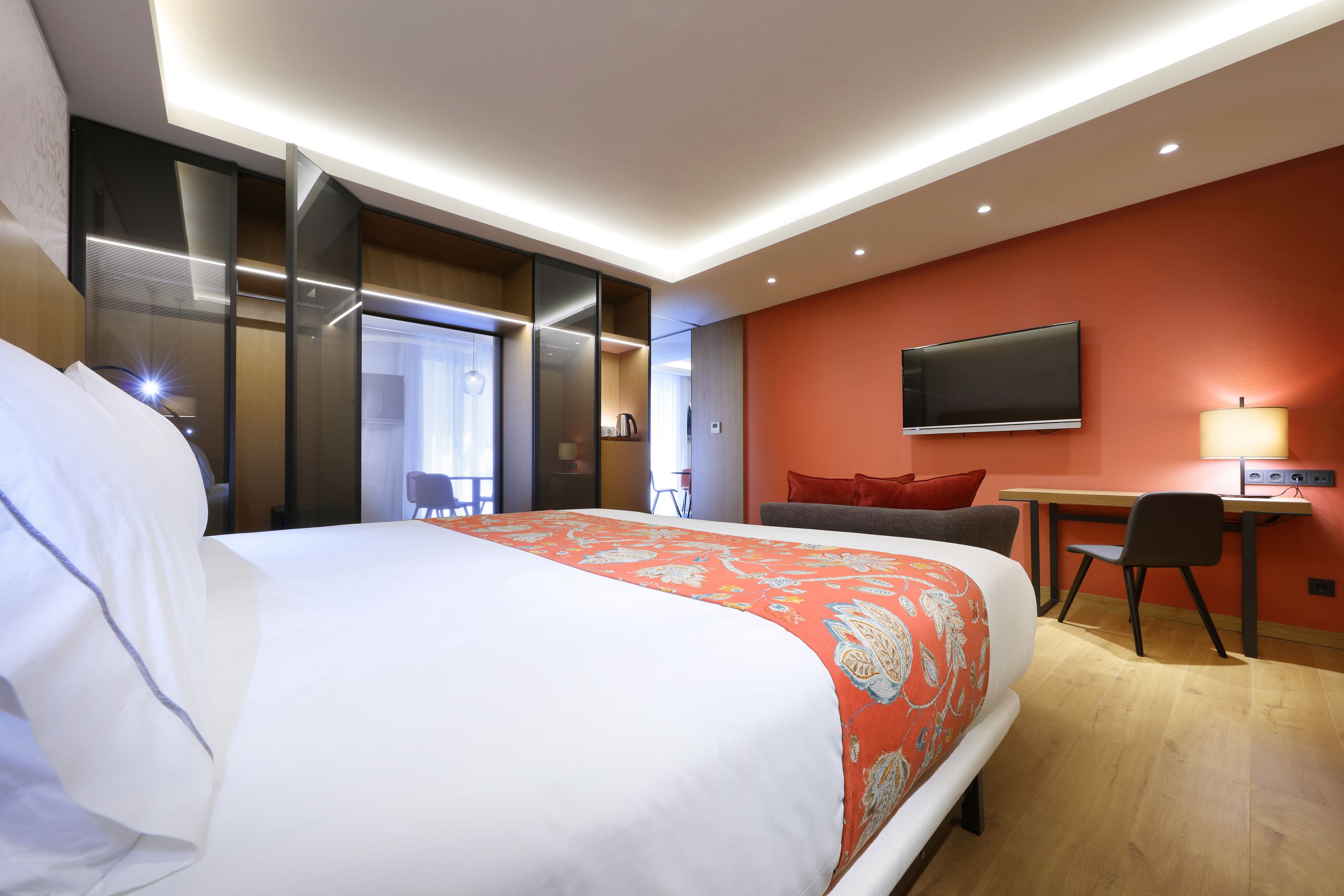 A hotel room with a large bed, a desk, a chair, a TV, and a window.