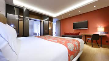 A hotel room with a large bed, a desk, a chair, a TV, and a window.