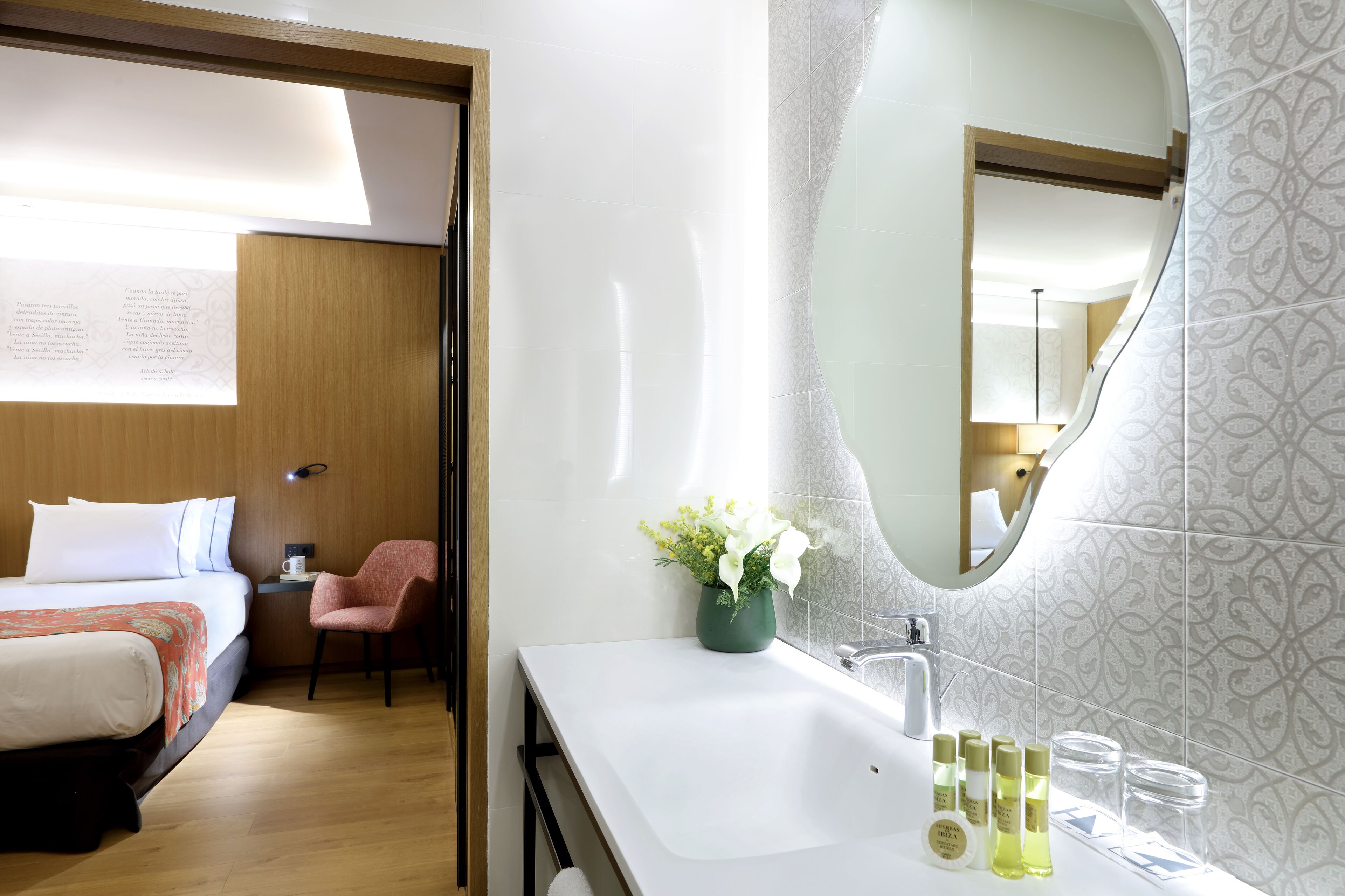 A hotel room with a bed, a chair, a sink, and a mirror.