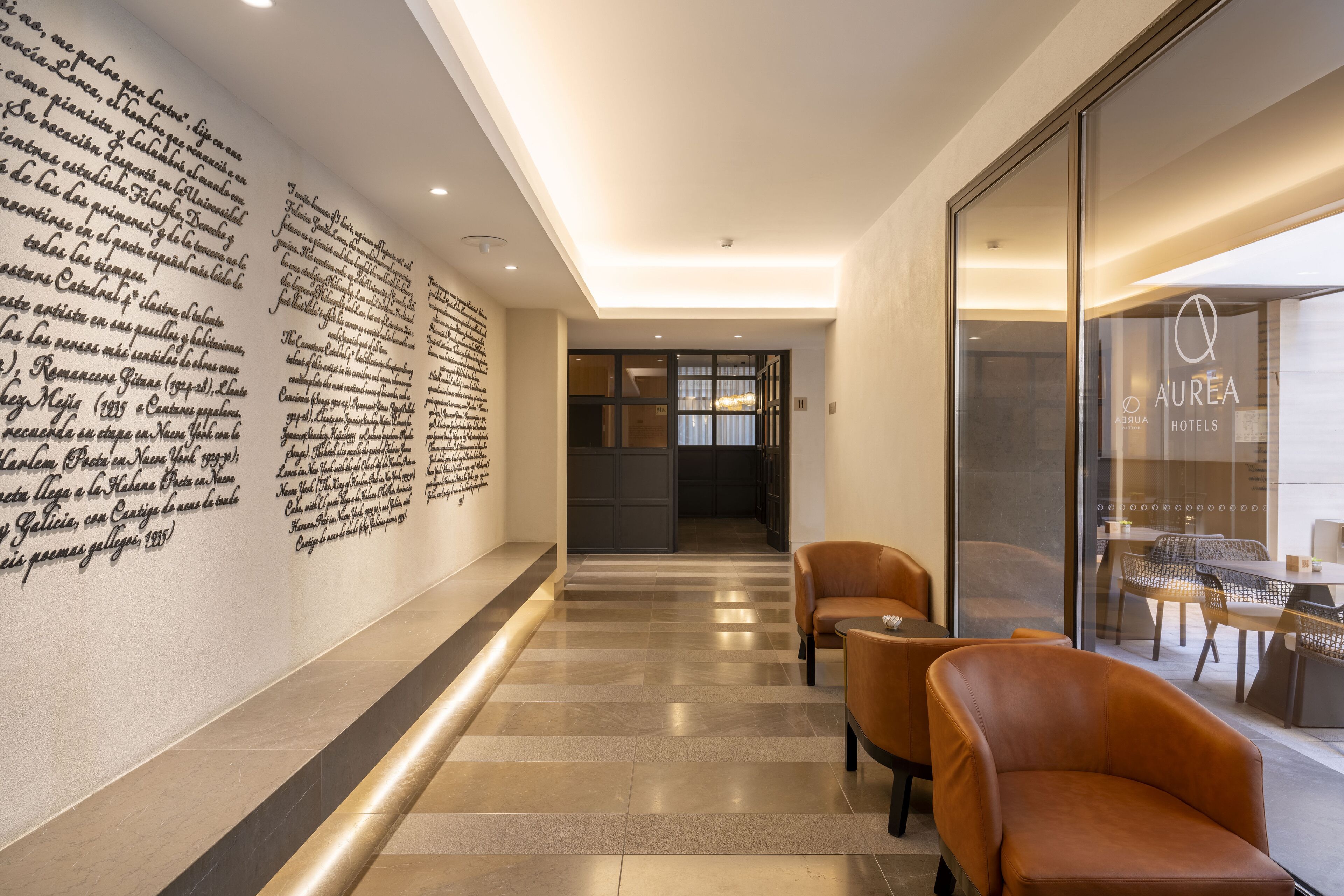A modern hotel lobby with a long wall of text, a glass door entrance, and leather seating.