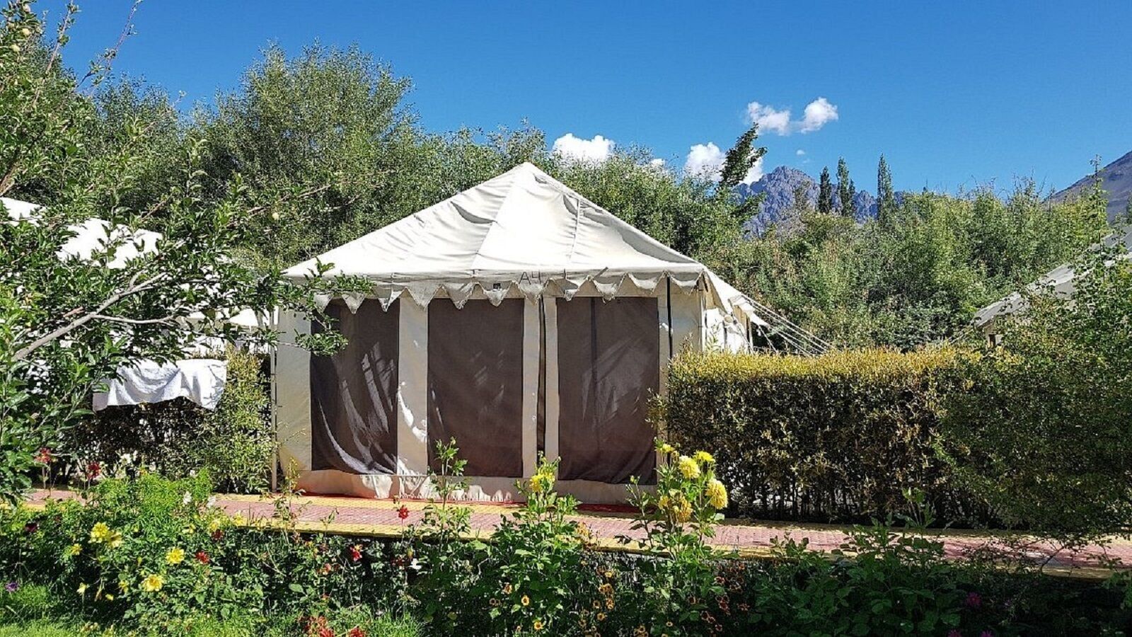 A white tent with a peaked roof, surrounded by lush greenery and a clear blue sky.