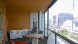 A balcony with a wooden floor, a cushioned sofa, a hanging chair, and a table with chairs.