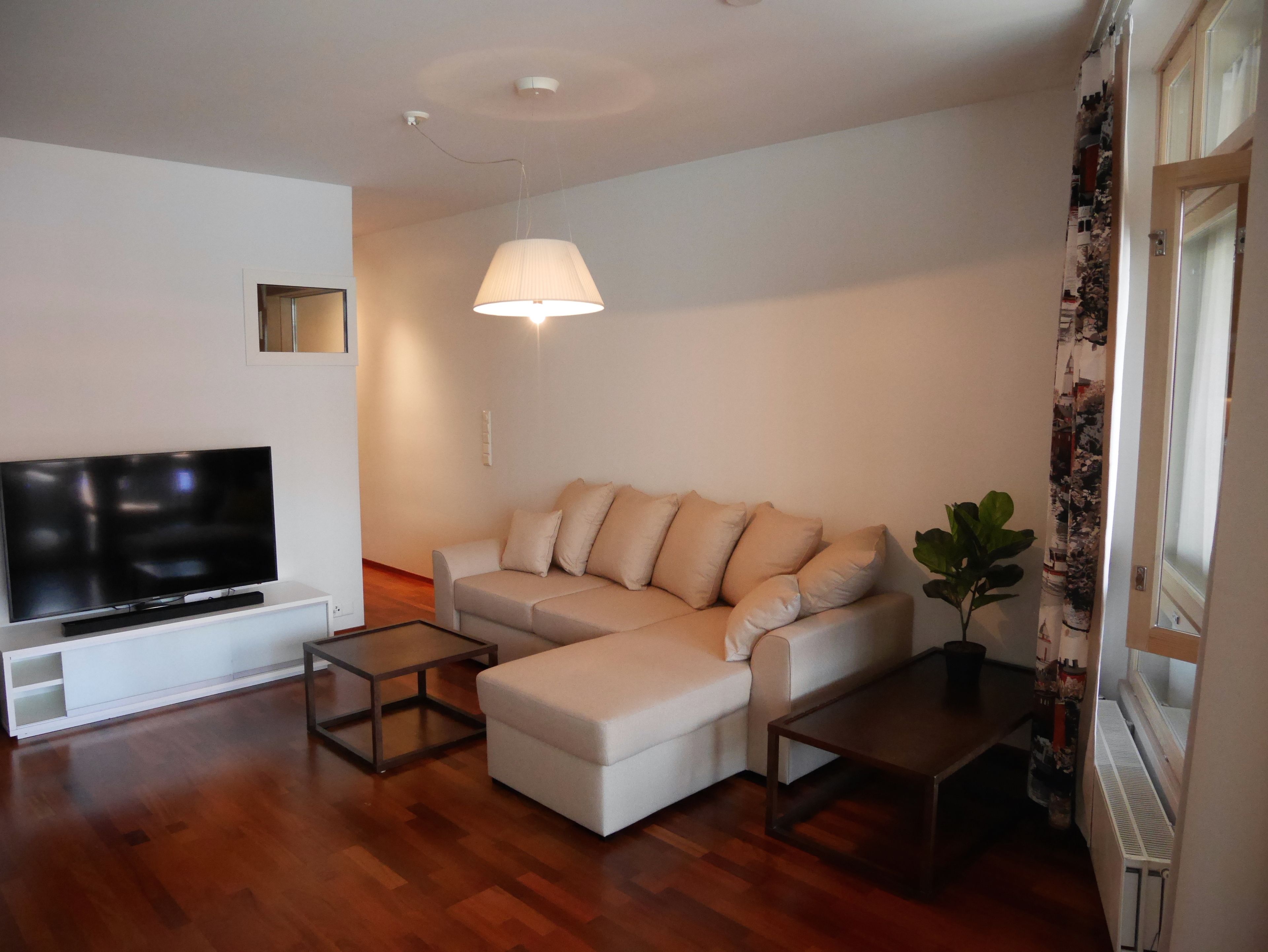 Una sala de estar moderna con un televisor de pantalla plana, un sofá, una mesa de centro y una lámpara colgante.