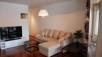 Una sala de estar moderna con un televisor de pantalla plana, un sofá, una mesa de centro y una lámpara colgante.