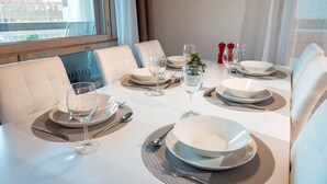 A dining table set with plates, glasses, and cutlery, with a view of a building outside.