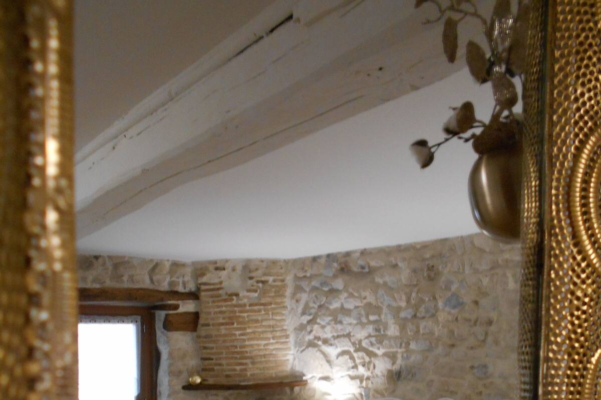 Une chambre avec un mur en pierre, un lit avec une literie à motifs, une lampe de chevet et une fenêtre.