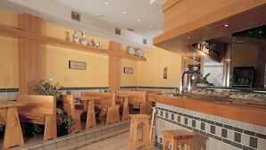 Un restaurante con mobiliario de madera, un salpicadero de azulejos y una zona de cocina visible al fondo.