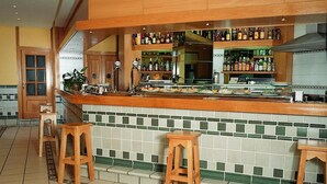 Una zona de bar con salpicadero de azulejos, taburetes de madera y una variedad de botellas en estantes.