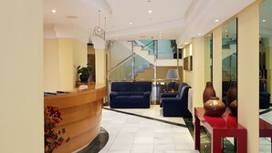 Un vestíbulo moderno con mostrador de recepción, zona de estar, escalera y paredes de vidrio.