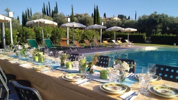 A poolside dining area with tables set for a meal, chairs, and umbrellas. - Gli Archi (Fauglia)
