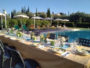 A poolside dining area with tables set for a meal, chairs, and umbrellas. - Gli Archi (Fauglia)