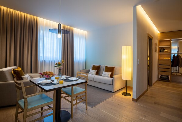 Una habitació d'hotel moderna amb zona de menjador, sofà i vestidor.