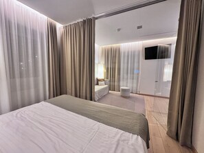 Habitació d'hotel moderna amb un llit gran, una zona de seients amb sofà i butaca, una taula rodona petita i una televisió.