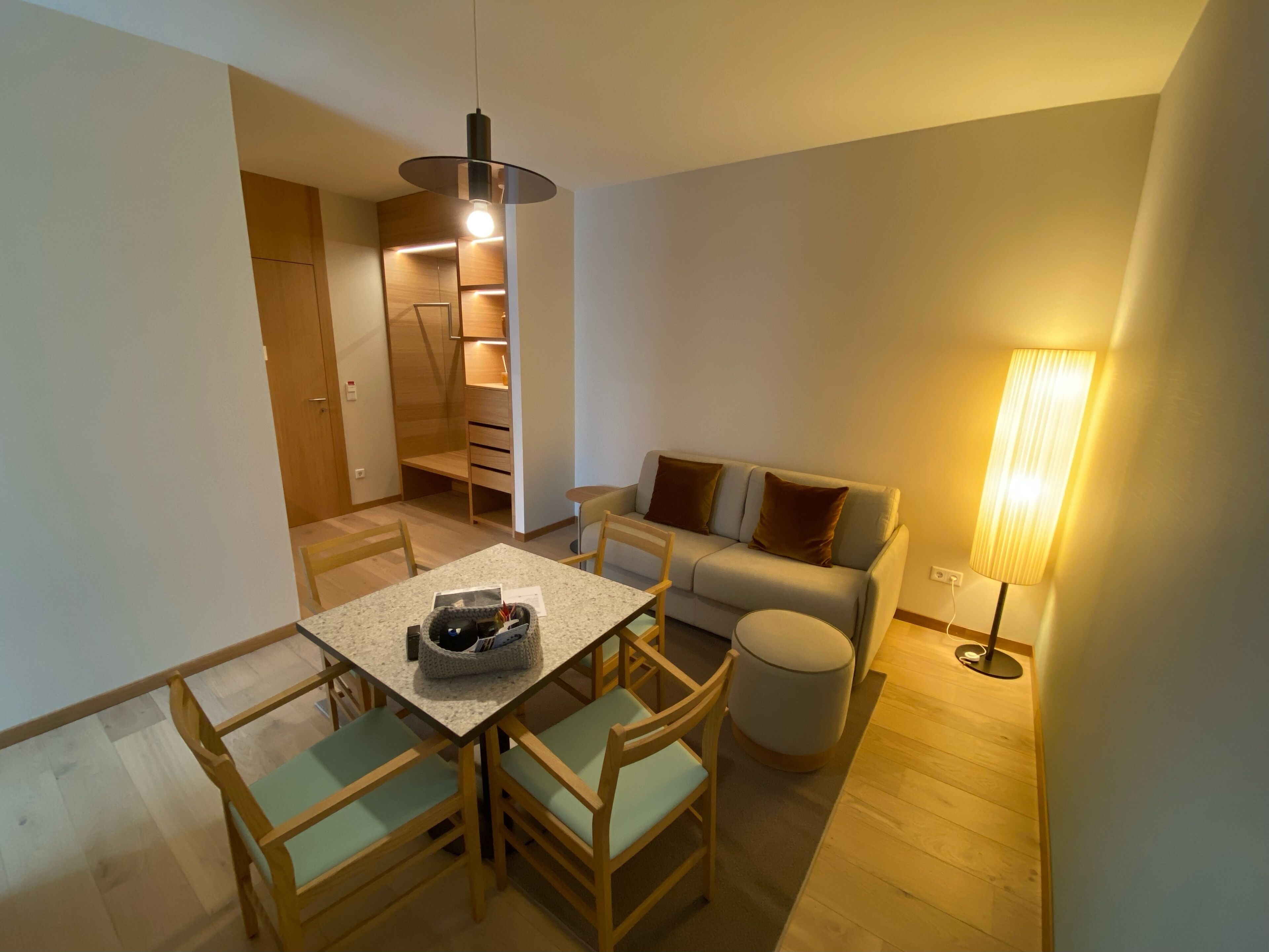 A compact living space with a dining table, chairs, a sofa, a lamp, and a built-in wardrobe.