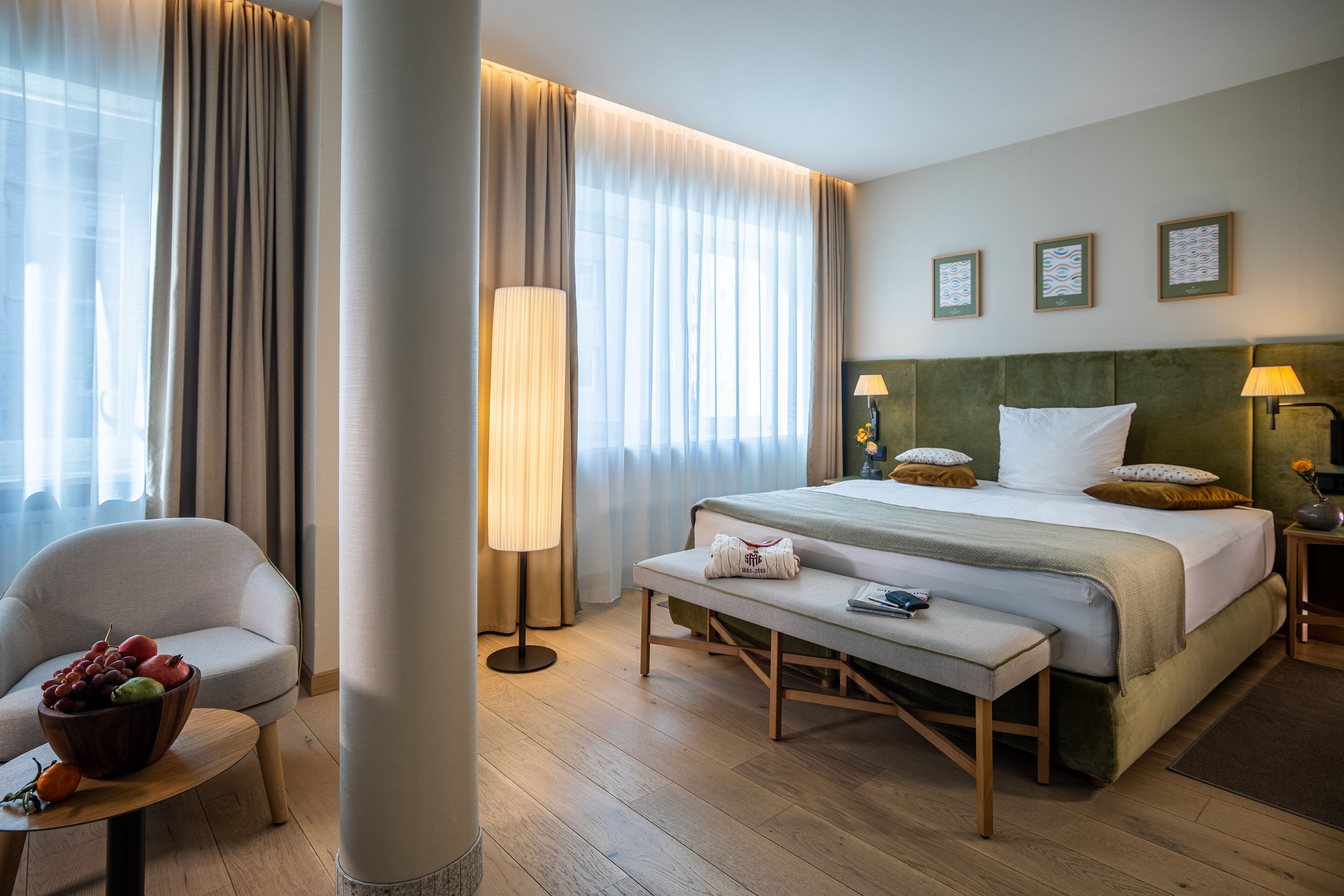Une chambre d’hôtel avec un lit, une table de chevet, une chaise, une lampe et une fenêtre avec des rideaux.