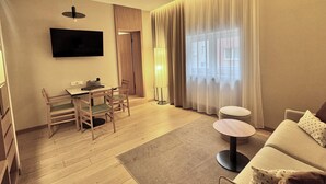 Una sala moderna con una televisión de pantalla plana, un comedor con mesa y sillas, un sofá y un amplio ventanal con cortinas.