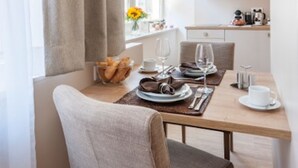 Un comedor con una mesa preparada para dos, una ventana con cortinas y una cocina al fondo.