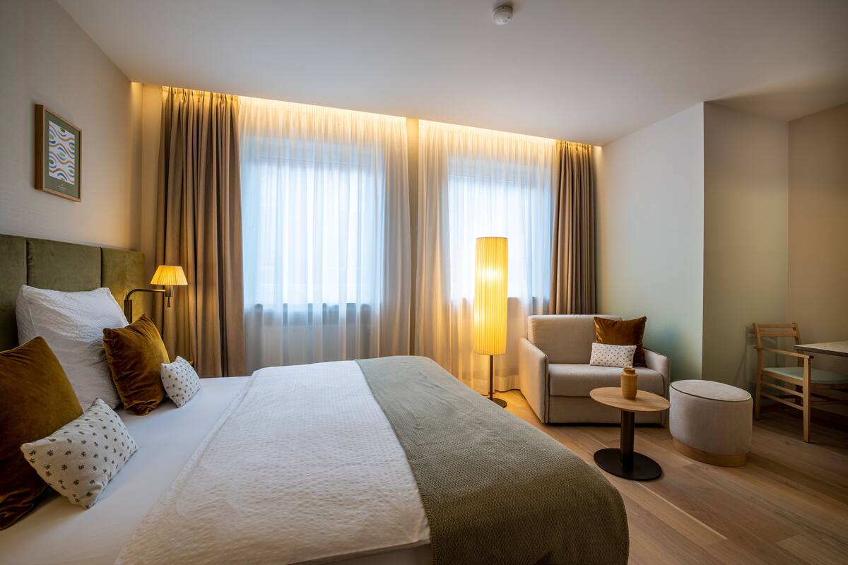 Hotellihuone, jossa on suuri sänky, sohva, pieni pyöreä pöytä ja tuoli.