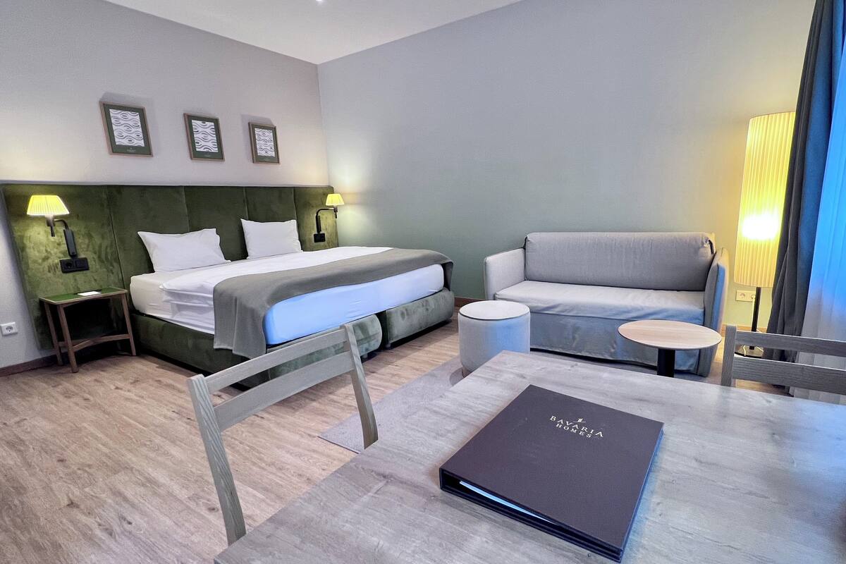 Moderni hotellihuone, jossa on sänky, sohva, pieni pöytä ja tuoli.