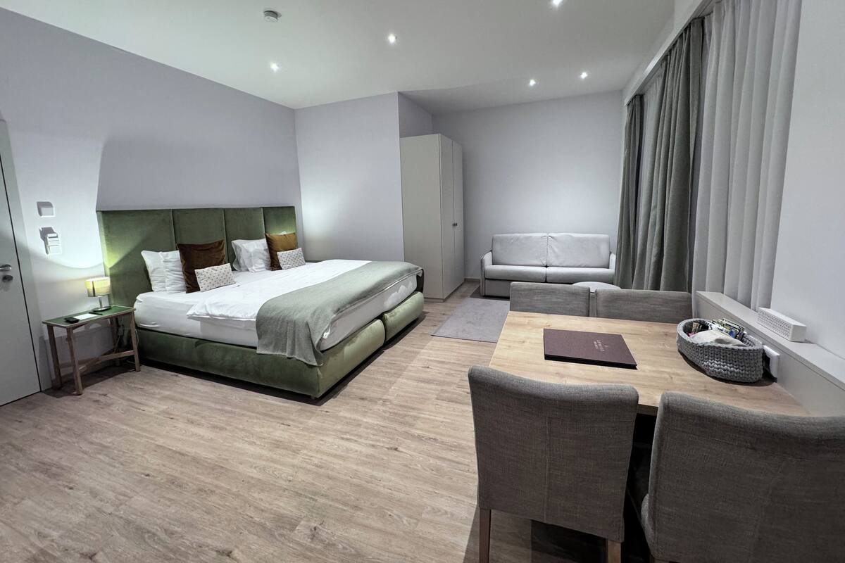 Moderni hotellihuone, jossa on suuri sänky, sohva, ruokapöytä ja ikkuna, jossa on verhot.