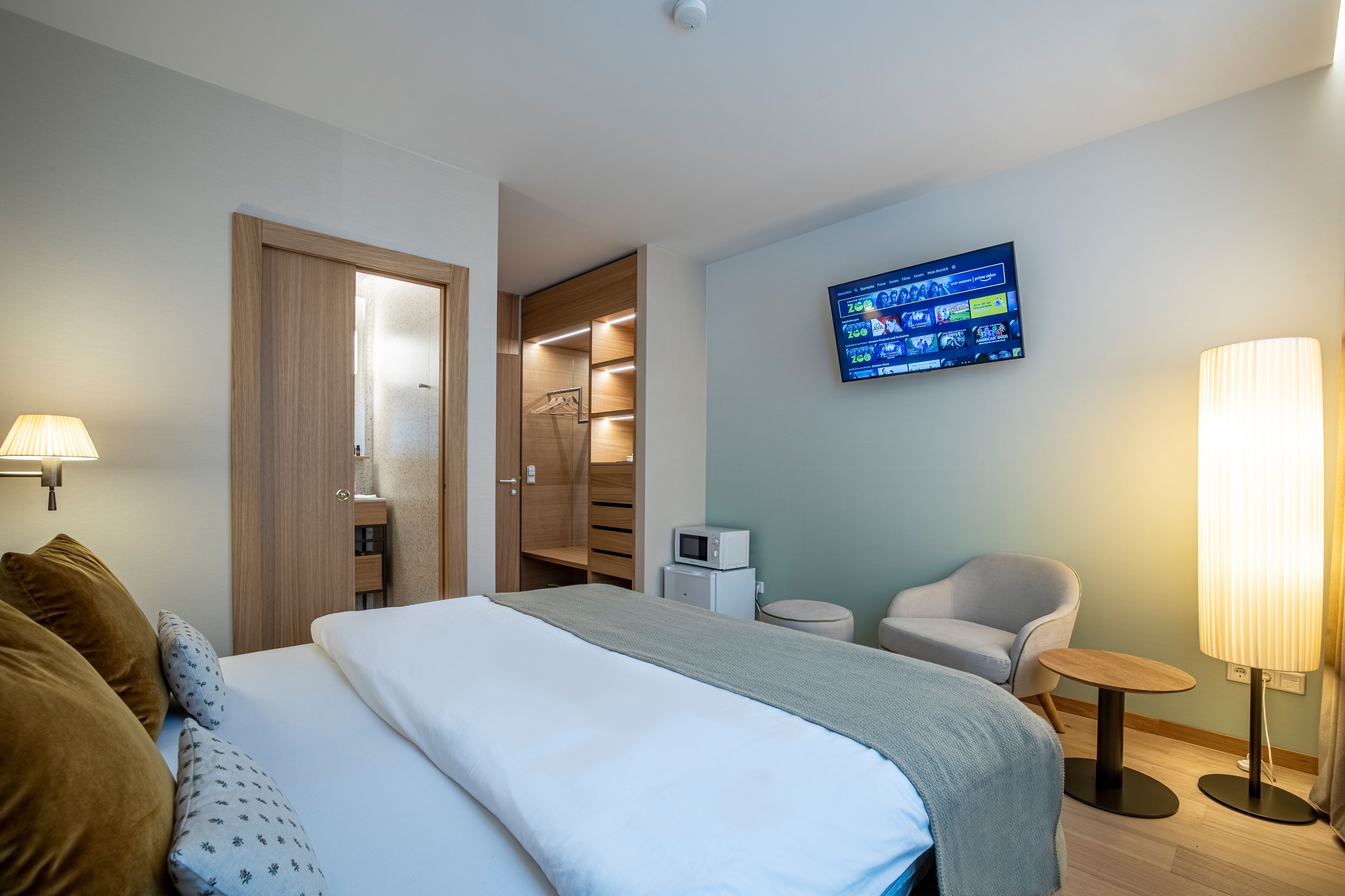 Une chambre d’hôtel avec un lit, un téléviseur fixé au mur, une chaise, une lampe et une petite table.