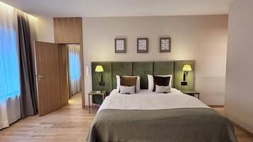 A hotel room with a large bed, two bedside tables with lamps, a door leading to another room, and a view of the outside.