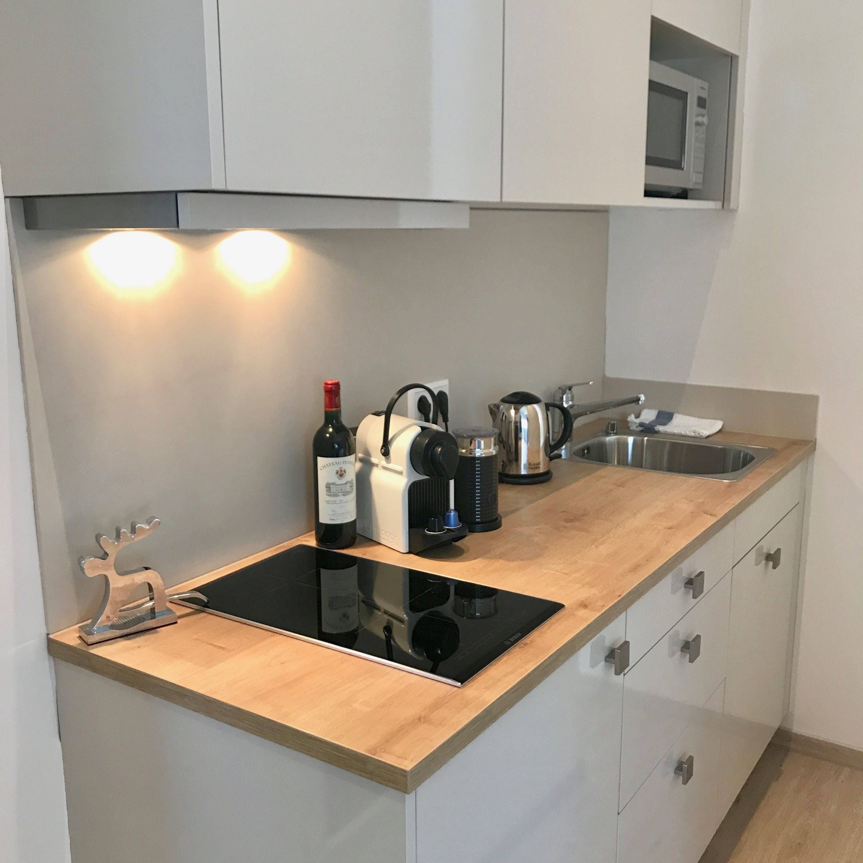 Eine moderne Küche mit integriertem Induktionskochfeld, einer Weinflasche, einer Kaffeemaschine und einem Wasserkocher.
