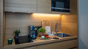Una cocina moderna con armarios de madera, un microondas integrado, un lavamanos y una encimera con una cafetera, una planta y productos frescos.