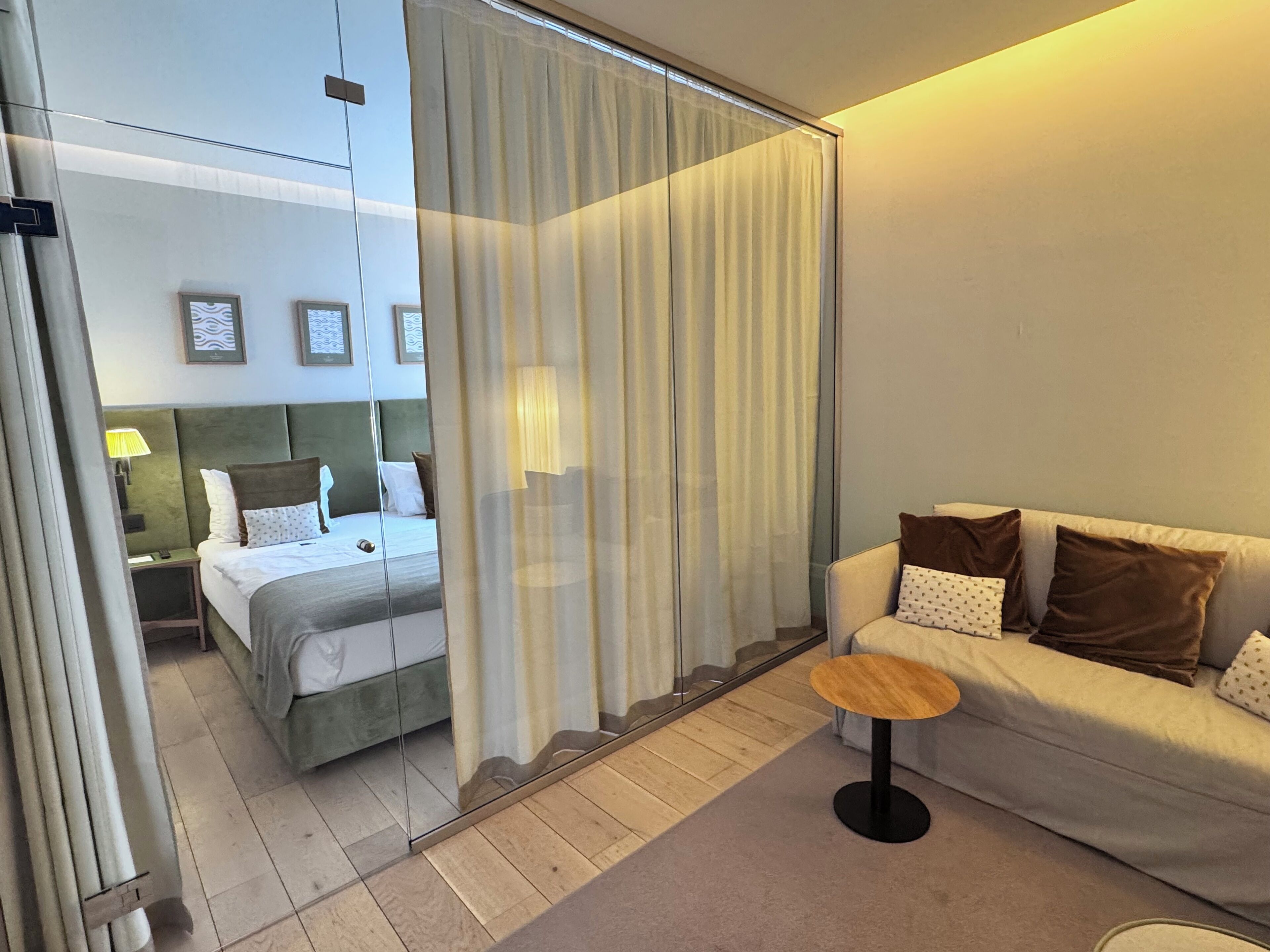 Una habitación de hotel con una cama, un sofá, una mesita y un separador de vidrio.