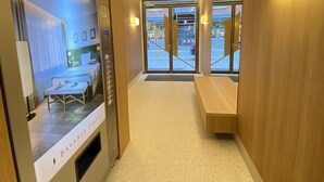 Un pasillo de hotel de diseño moderno, con una zona de recepción que incluye una pantalla digital y un área de estar con un banco.