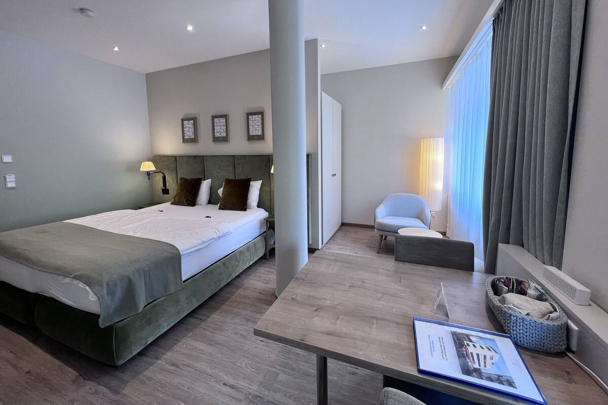 Moderni hotellihuone, jossa on suuri sänky, työpöytä, tuoli ja näkymä kaupunkiin.
